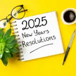 A notepad with '2025 New Year's Resolutions' written on it, accompanied by a pen, glasses, a plant, and a cup of coffee—symbolizing planning and reflection for psychotherapists exploring the best therapy training programs in 2025