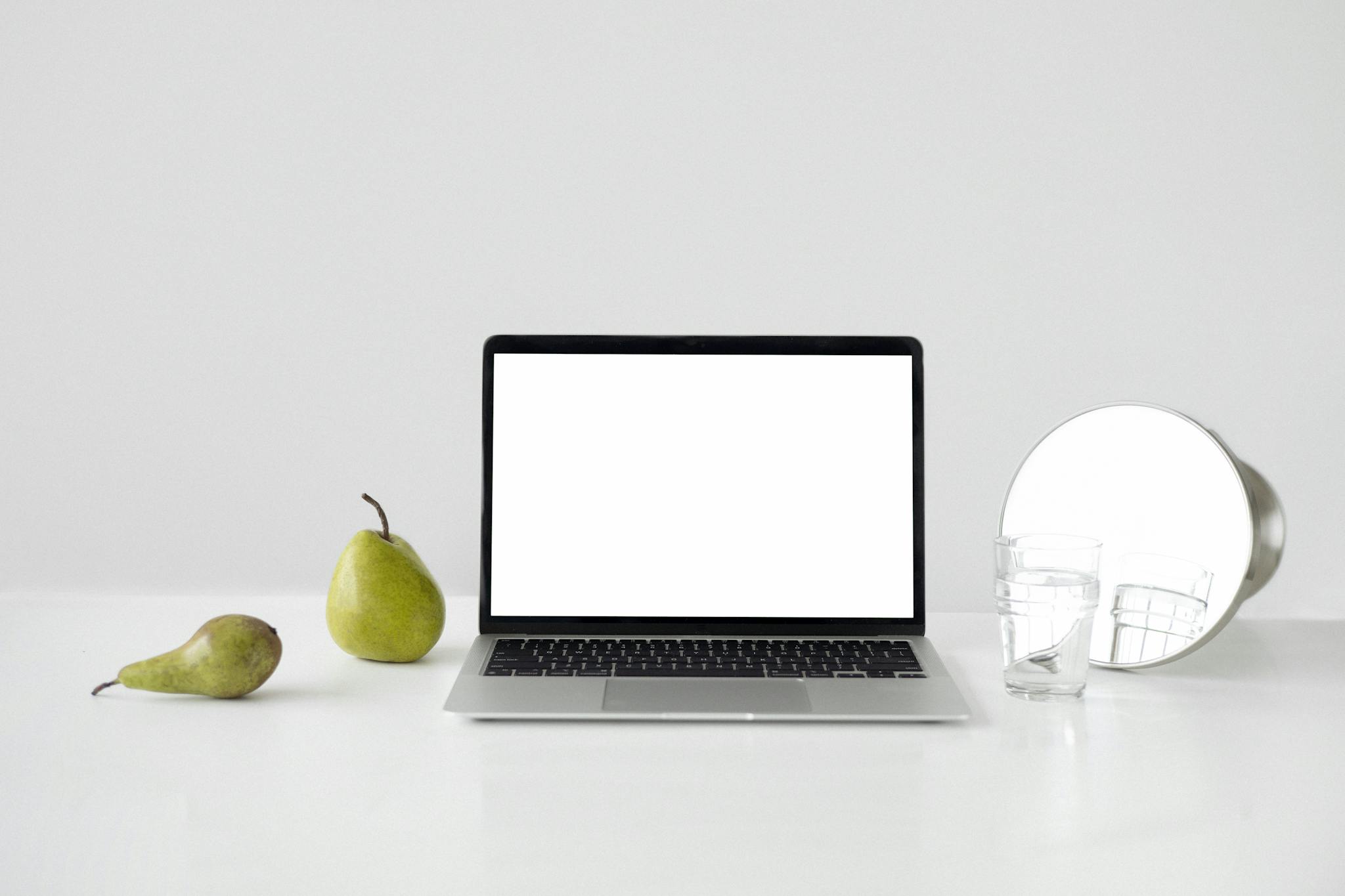 A minimalist desk setup featuring a laptop, pears, and a mirror for a modern look.