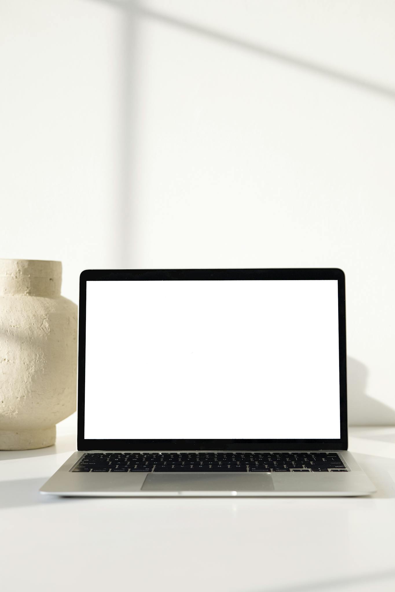 Modern workspace featuring a blank laptop screen and clay pot, ideal for tech and design themes.